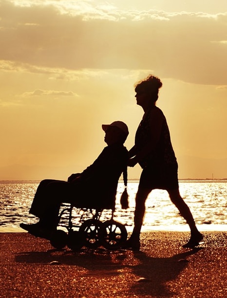a man in a wheelchair being pushed by a carer at sunset by the ocean