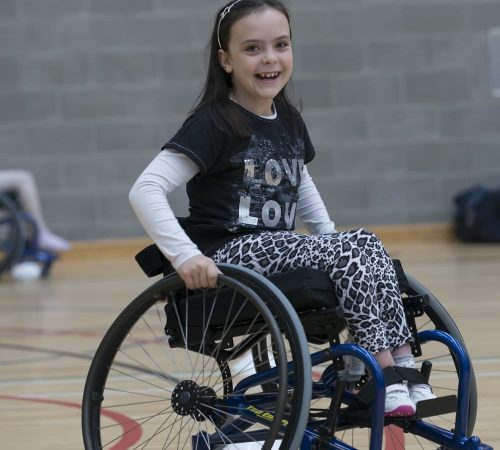 A child playing on a basketball court in a wheelchair